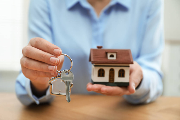 Real estate agent holding house model and key at wooden table, closeup - Foto, immagini