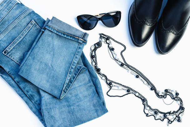 Overhead view of womans casual outfit on white background - glasses, blue jeans, necklace and leather chelsea boots. Flat lay, top view, copy space. Trendy, minimal hipster look. - Photo, Image