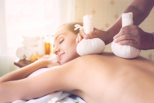 Kuuroord salon. Masseur massage klant terug met behulp van warme kruidenbal in spa salon kamer in luxe resort. Mooie jonge vrouw voelt zich ontspannen, rustig. Spa naakte lichaam massage behandeling, hete kruidenbal  - Foto, afbeelding