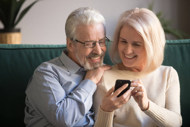 Mature attractive couple sitting on couch using smartphone - Zdjęcie, obraz
