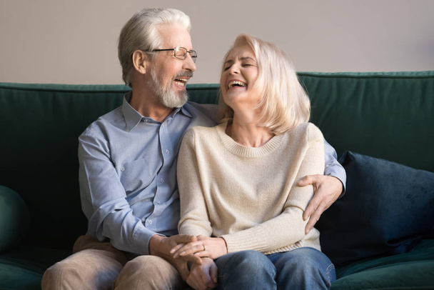 Overjoyed laughing senior couple embracing sitting on couch - Foto, afbeelding