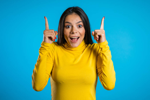 Smiling happy student girl showing eureka gesture. Portrait of young thinking pondering business woman having idea moment pointing finger up on blue background - Fotoğraf, Görsel