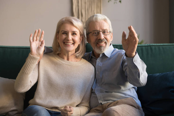 Happy elderly couple looks at camera waving hands greeting friend - Foto, afbeelding