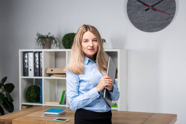 Businesswoman Holding Large File. young womanl standing in the office and holding folder. Portrait of young office worker holding folders of paperwork while standing in modern office - Zdjęcie, obraz