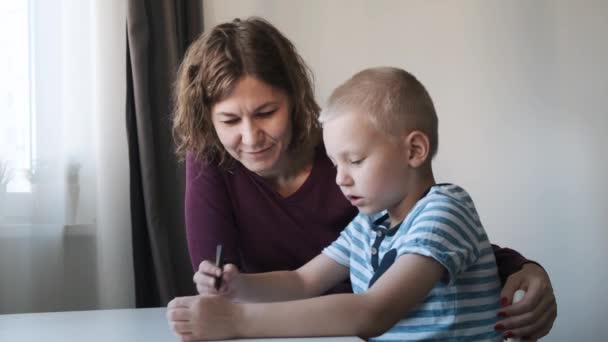Child boy sitting at the table at home and drawing together with their mom. Family concept - Materiał filmowy, wideo