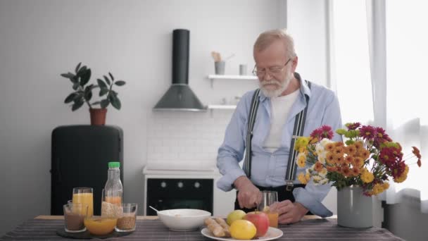 Großeltern, fürsorglicher Großvater mit Bart und Sehbrille bereitet Vitaminspeise für sich und seine lächelnde Enkelin zu, die am Tisch steht - Filmmaterial, Video