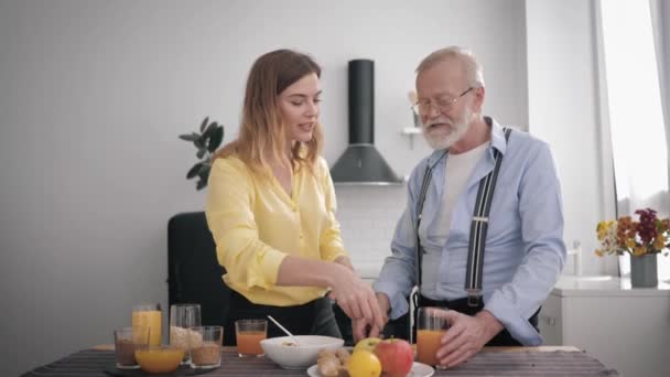 family relationships, smiling adult girl helps her old grandfather prepare vitamin salad from healthy products while having fun together in kitchen - Video, Çekim