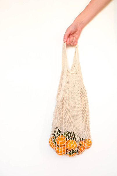 A human hand holds a string bag with tangerines on white background. - Valokuva, kuva