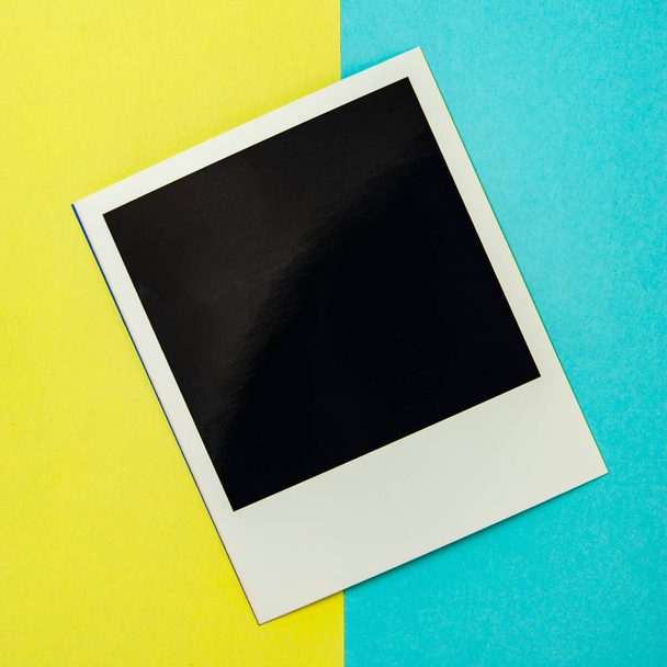 Old black square photo on white lying on a yellow and blue backg - Foto, Imagem