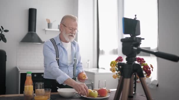 egészséges ételek, egy szakállas és látásjavító szemüveges idős férfi megfelelő táplálkozást javasol, és különböző gabonaféléket mutat be az asztalnál a konyhában. - Felvétel, videó