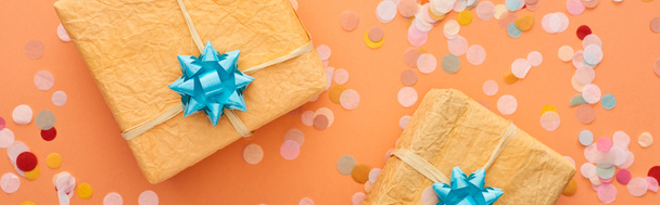 Prise de vue panoramique des arcs bleus sur les boîtes cadeaux près des confettis sur orange
  - Photo, image