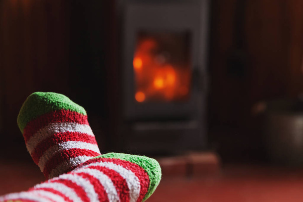 Feet legs in winter clothes wool socks at fireplace at home on winter or autumn evening relaxing and warming up - Фото, изображение