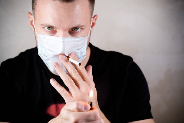 a man in a medical protective mask with a sad look about to smoke - Φωτογραφία, εικόνα