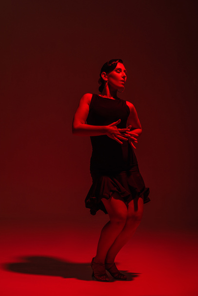 bailarina apasionada en vestido negro realizando tango sobre fondo oscuro con iluminación roja
 - Foto, imagen
