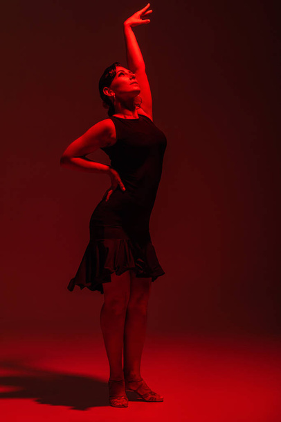 elegante bailarina en vestido negro realizando tango sobre fondo oscuro con iluminación roja
 - Foto, imagen