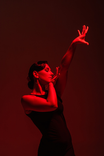 hermosa bailarina en vestido negro realizando tango sobre fondo oscuro con iluminación roja
 - Foto, imagen