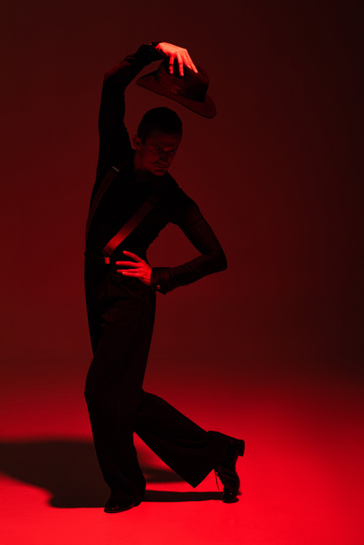elegáns táncos tartja kalap feje felett, miközben végre tangó sötét háttér piros világítás - Fotó, kép