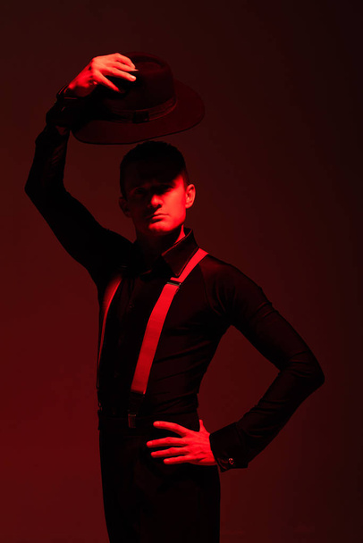 expresiva bailarina de tango mirando a la cámara y sosteniendo el sombrero sobre la cabeza sobre fondo oscuro con luz roja
 - Foto, imagen