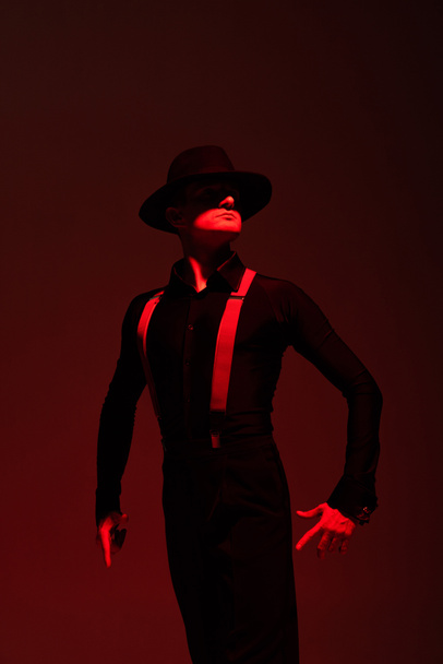 expressive dancer in black clothing and hat performing tango on dark background with lighting - Photo, Image