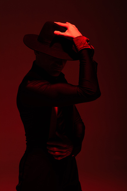 bailarina expresiva en ropa negra y sombrero realizando tango sobre fondo oscuro con iluminación roja
 - Foto, Imagen