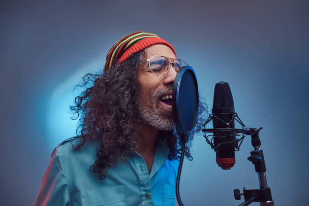 African Rastafarian singer male wearing a blue shirt and beanie emotionally writing song in the recording studio. - Photo, Image