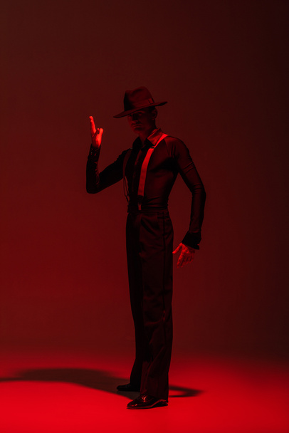 élégante danseuse au chapeau noir exécutant le tango sur fond sombre avec éclairage rouge
 - Photo, image
