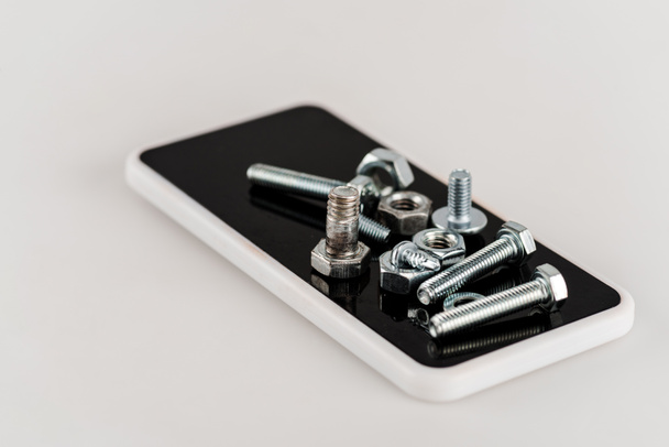tornillos y pernos metálicos en el teléfono inteligente sobre fondo blanco
 - Foto, Imagen