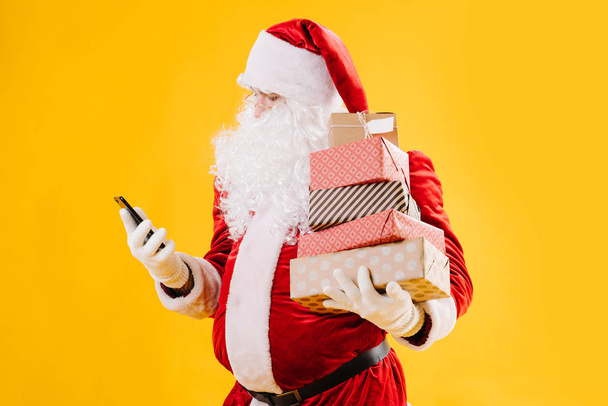 Santa Claus mirando el teléfono con muchos regalos en cajas
 - Foto, Imagen