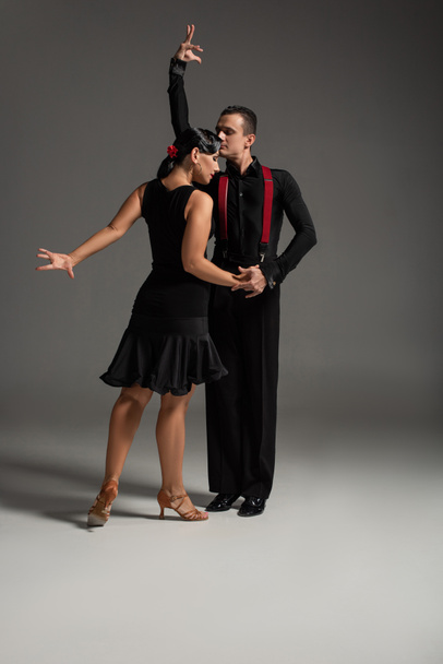 two expressive dancers in black clothing performing tango on grey background - Photo, Image