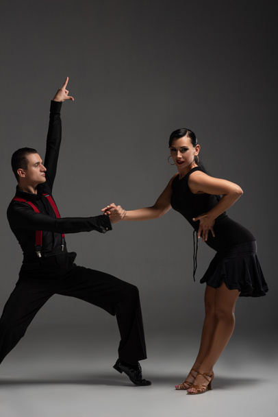 ilmeikäs pari tanssijaa mustissa vaatteissa suorittamassa tangoa harmaalla taustalla
 - Valokuva, kuva