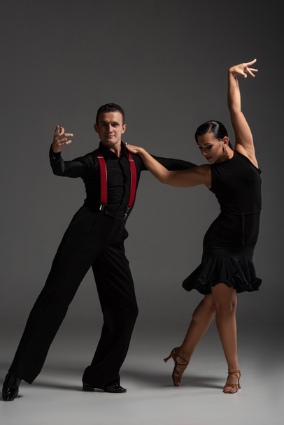 aistillinen pari tanssijoita mustissa vaatteissa suorittaa tango harmaalla taustalla
 - Valokuva, kuva