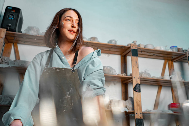 Beautiful Girl Relaxing on Weekend Ceramics Master Class and standing near shelving with Clay Wares - 写真・画像