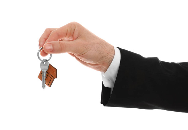 Μεσίτης ακινήτων κρατώντας κλειδί σπίτι με μπιχλιμπίδι σε λευκό φόντο, closeup - Φωτογραφία, εικόνα