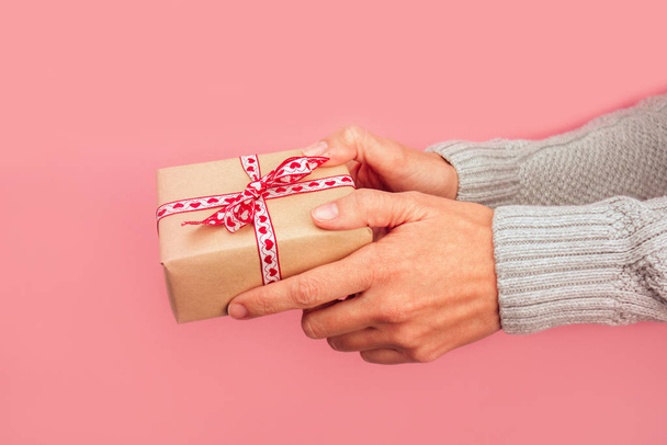 Woman's hands giving a gift with a bow of hearts on a pink background.  Christmas, new year, birthday, valentine's day, mother's day concept. - Photo, Image