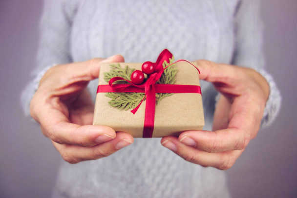 Γυναίκα με γκρι πουλόβερ κρατώντας ένα μικρό χριστουγεννιάτικο δώρο. - Φωτογραφία, εικόνα