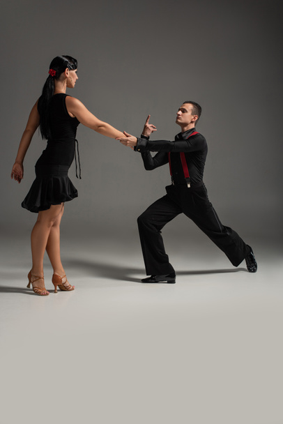expressive couple of dancers in black clothing performing tango on grey background - Foto, imagen