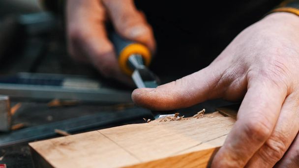 Carpentry indoors - a woodworker cutting out the recess on the wooden block with a chisel - Фото, изображение