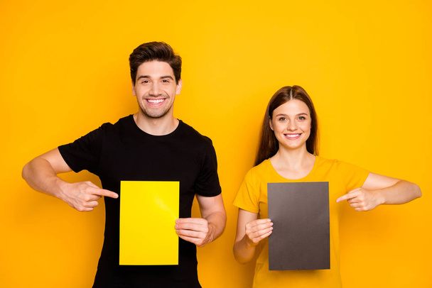 Photo of cheerful positive cute pretty sweet gorgeous two people working as advertisers together pointing at empty sheets of paper with forefingers isolated over vibrant color yellow background - Fotografie, Obrázek