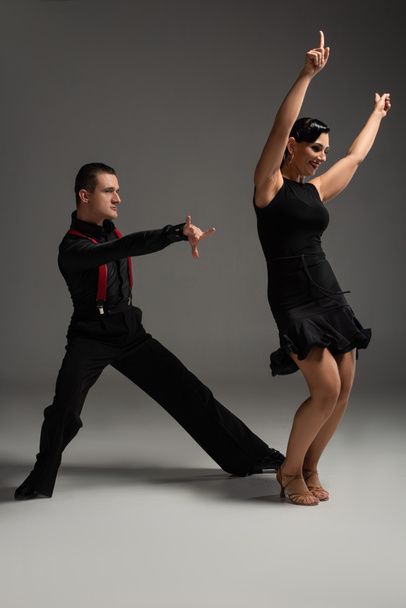 sensual couple of dancers in black clothing performing tango on grey background - Foto, afbeelding