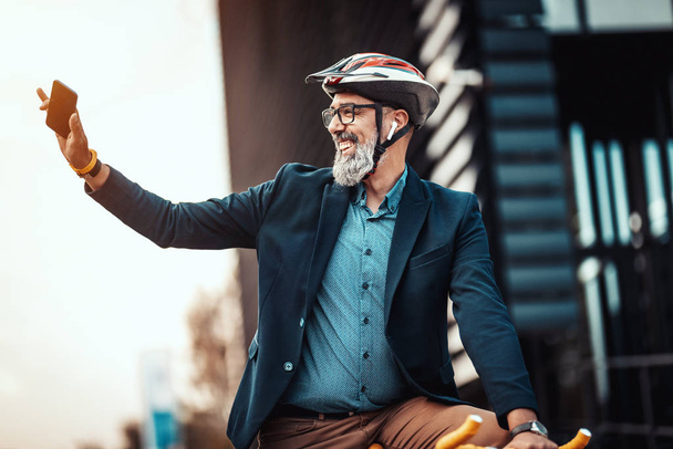 lässig gut aussehender Geschäftsmann mittleren Alters fährt mit dem Fahrrad zur Arbeit und grüßt jemanden vor dem Büroviertel. - Foto, Bild