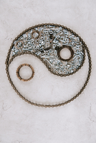 vista superior de engrenagens e parafusos metálicos envelhecidos dispostos em símbolo taijitu no fundo cinza
 - Foto, Imagem