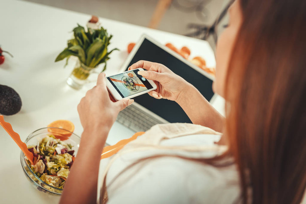 schöne junge Frau macht Foto von gesundem Salat mit Smartphone für ihren vlog. - Foto, Bild