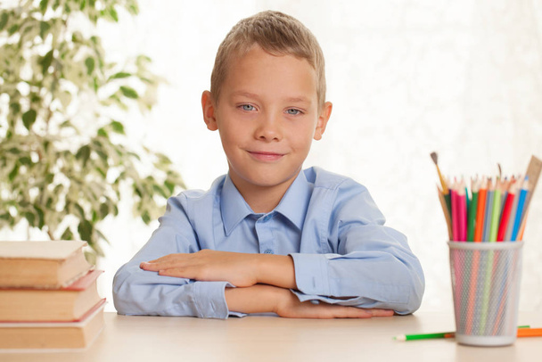 Молодой школьник сидит за столом и собирается делать домашнее задание. Концепция начального образования
 - Фото, изображение