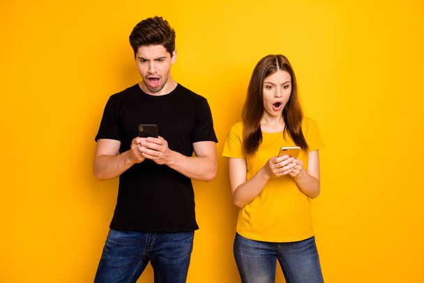 Photo of chatting browsing sad upset negative dissatisfied disappointed couple suspecting each other of betrayal wearing jeans denim black t-shirt isolated vivid color yellow background - Zdjęcie, obraz