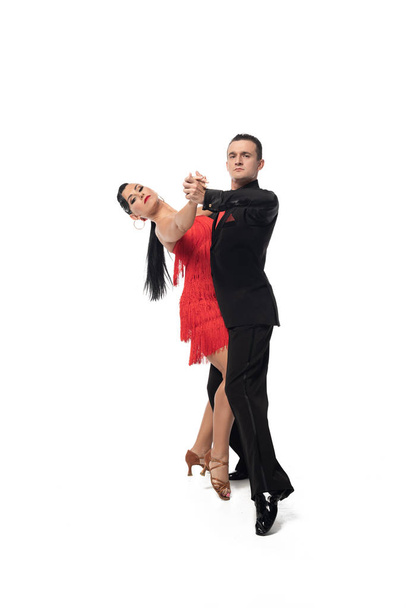 Paar eleganter Tänzer, die in die Kamera schauen, während sie Tango auf weißem Hintergrund tanzen - Foto, Bild