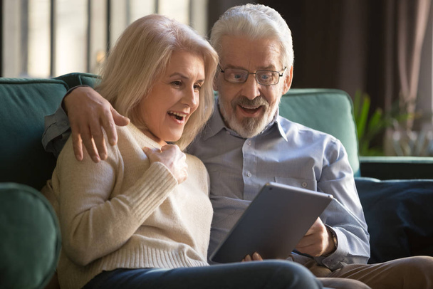 Happy amazed elderly couple looking at digital tablet screen - Valokuva, kuva