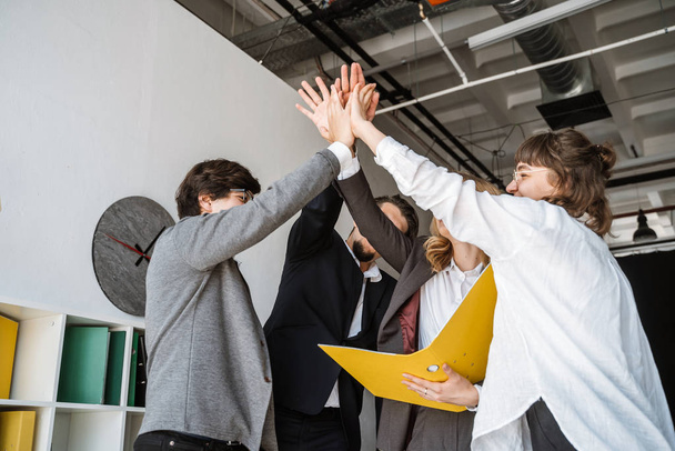 Vrolijke jonge groep mensen staan in het kantoor en geven high five - Foto, afbeelding
