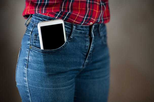 a large smartphone sticks out of a pocket tight-fitting girls jeans - 写真・画像