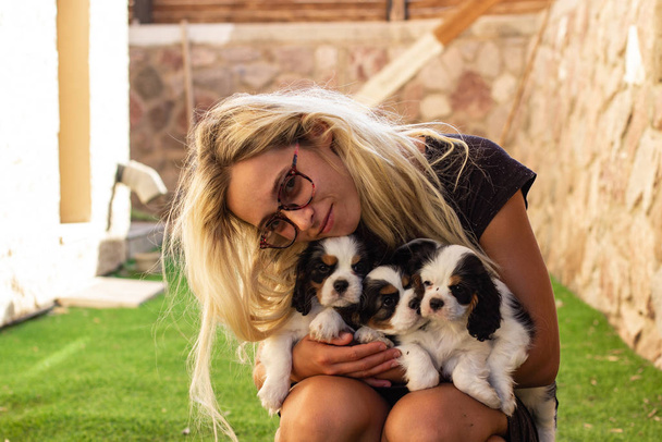 glad woman without make up holding black and white King Charles Cavalier dog cute puppies in outdoor domestic back yard sunny space  - Фото, зображення