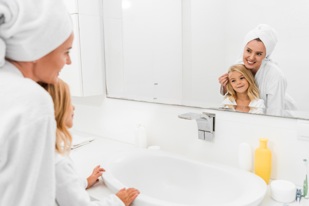 boldog gyerek és vonzó anya néz tükör a fürdőszobában  - Fotó, kép